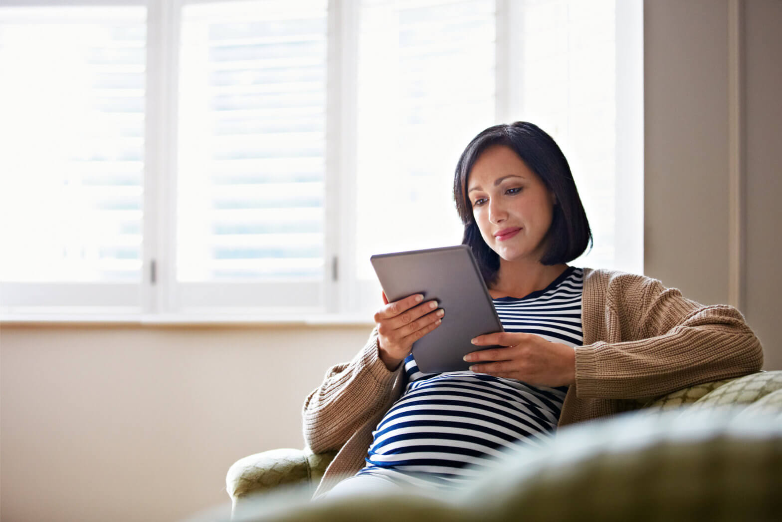 Shot of a pregnant woman sitting on her sofa using a digital tablet